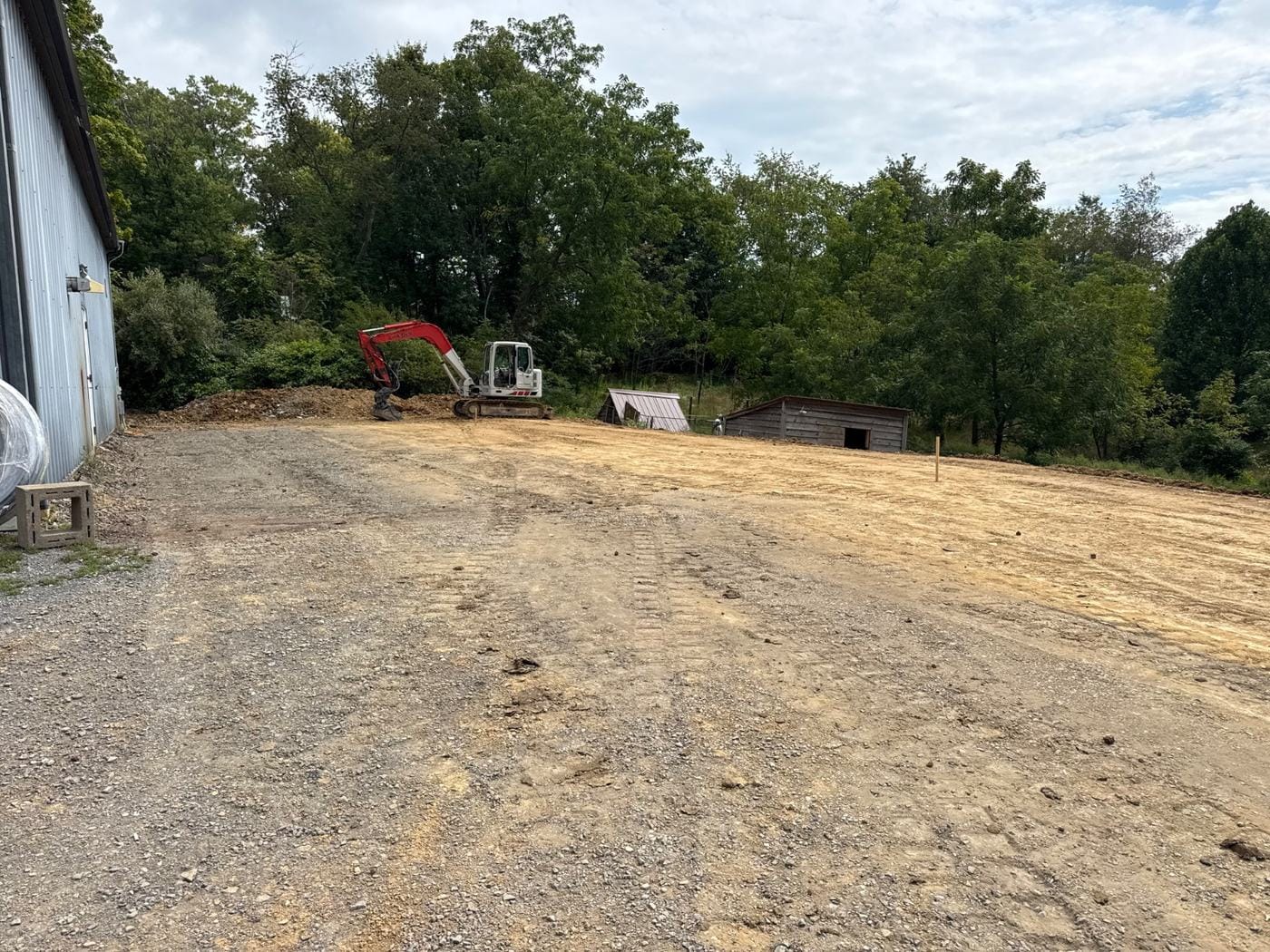 A wide graded yard, with the excavator back at the tree line.