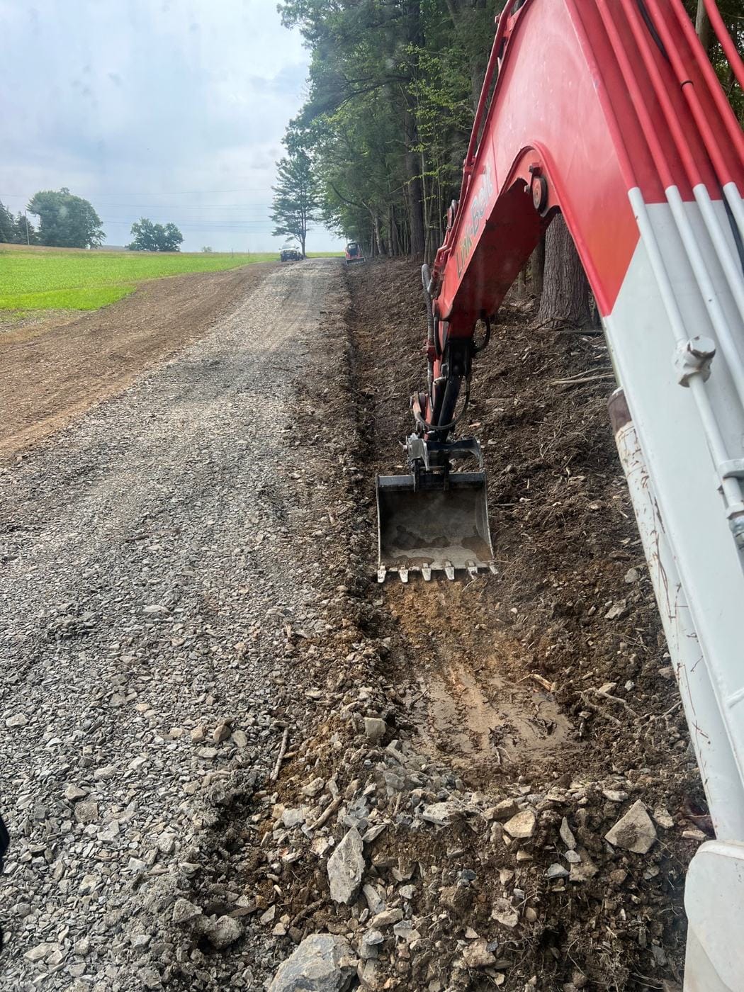 An excavator digging a ditch beside a gravel road.