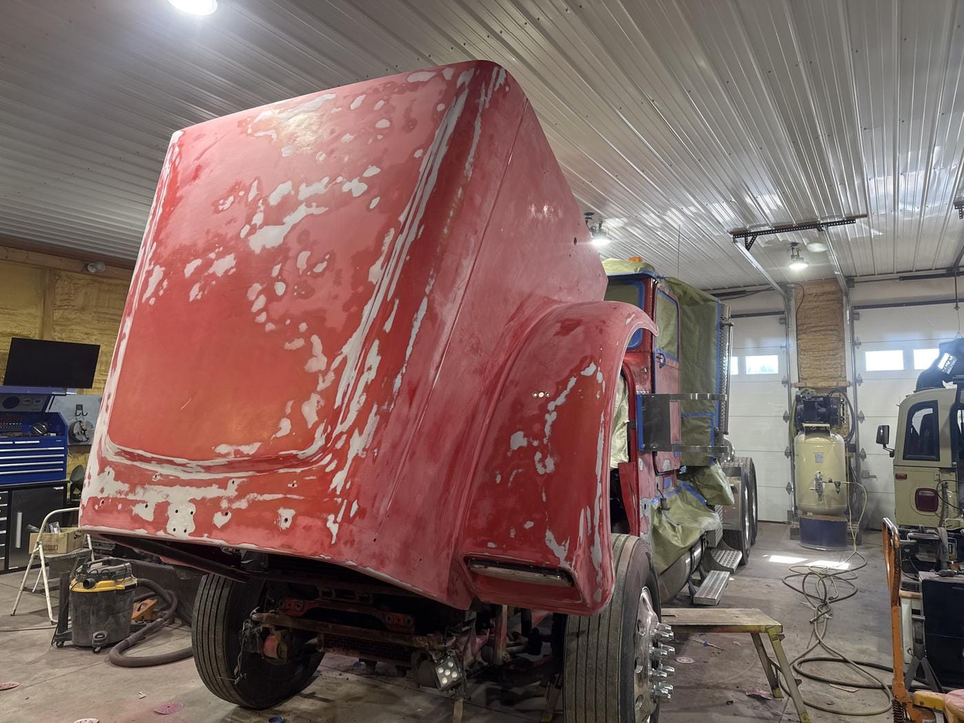 A red hood sanded down for bodywork, still on the truck.