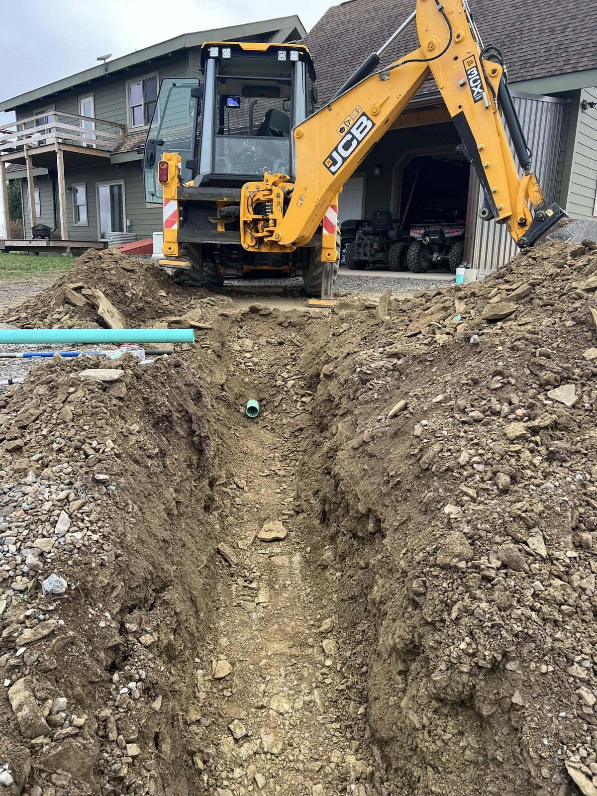 An open trench with pipe laid in, and the backhoe by the house.