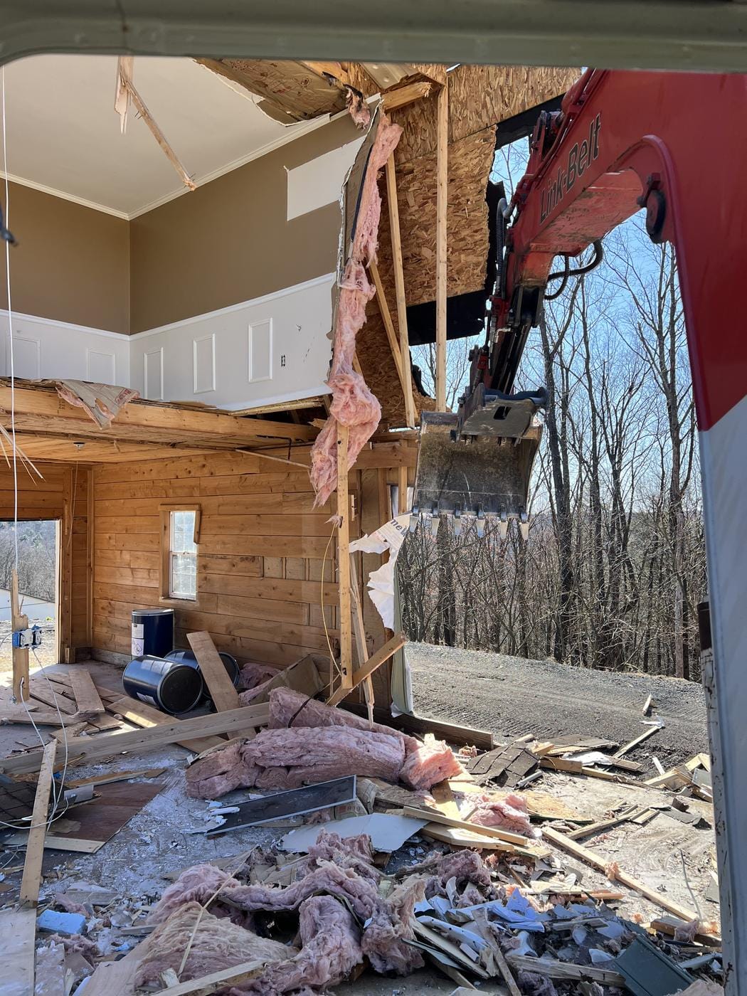 Looking into a building mid tear-down, with the excavator at right.